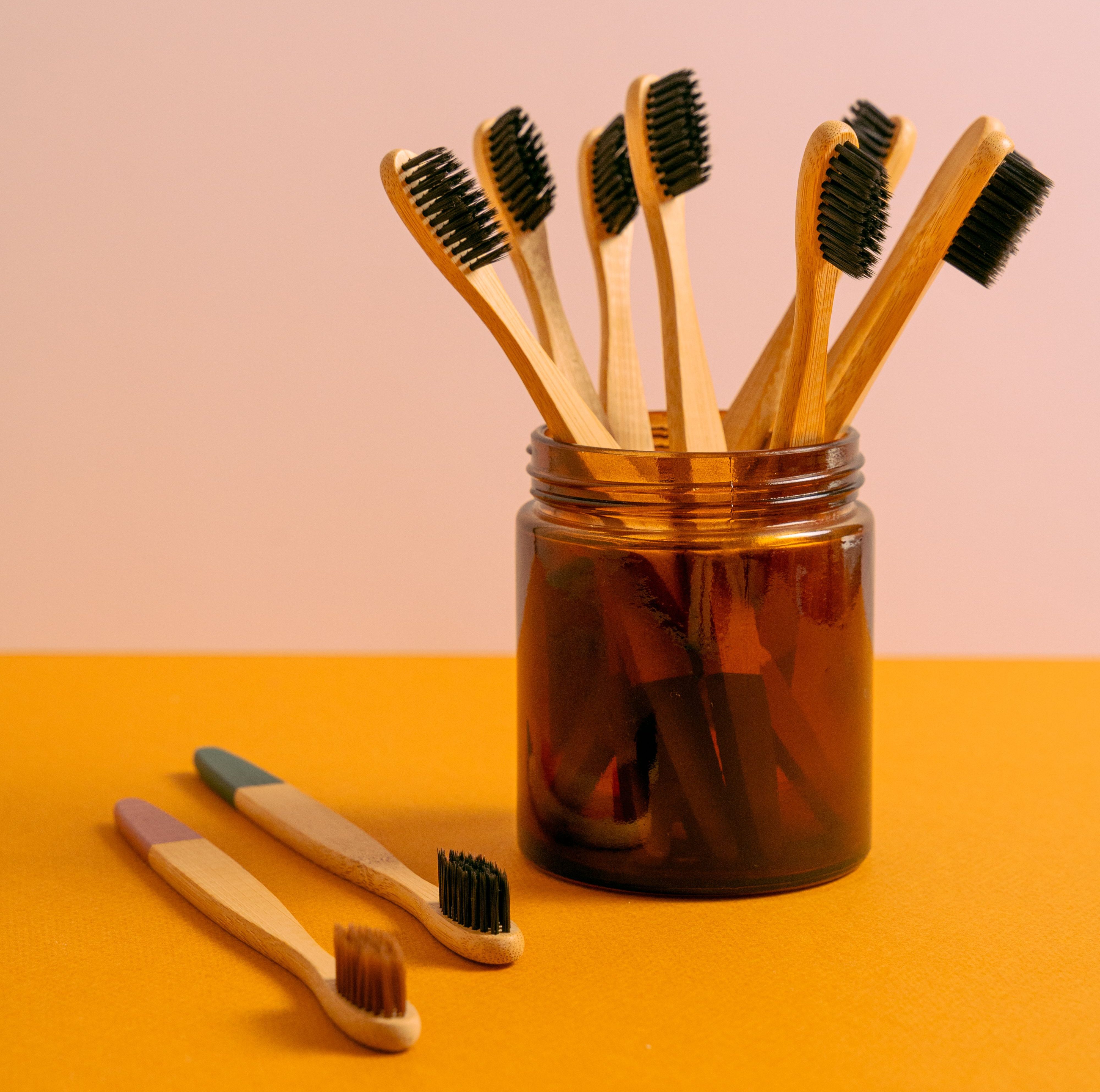 A collection of toothbrushes, seven of them in a small jar and two on a countertop. The brush handles are wooden and most of them have black brushes.